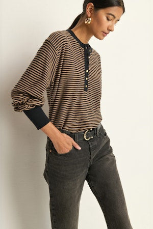 Woman wearing a striped sweater and dark jeans against a plain background