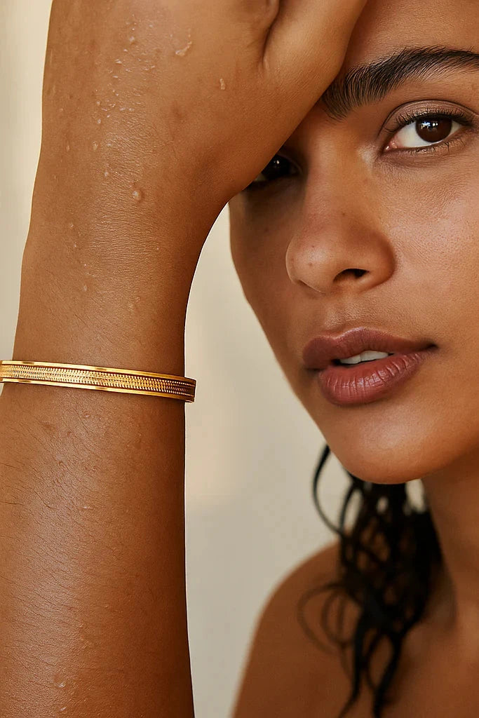 Close-up of a woman with a gold bracelet on her wrist against a neutral background