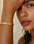 Close-up of a woman with a gold bracelet on her wrist against a neutral background