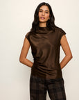 Woman wearing a brown cowl-neck top and plaid pants against a white background