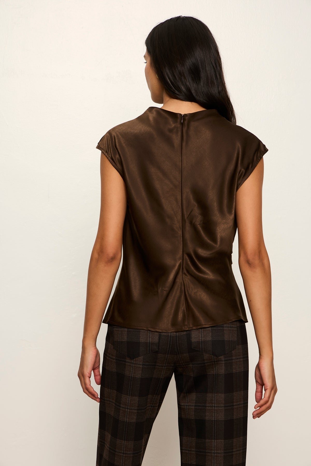 Person wearing a brown sleeveless top and plaid pants against a white background