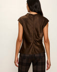 Person wearing a brown sleeveless top and plaid pants against a white background