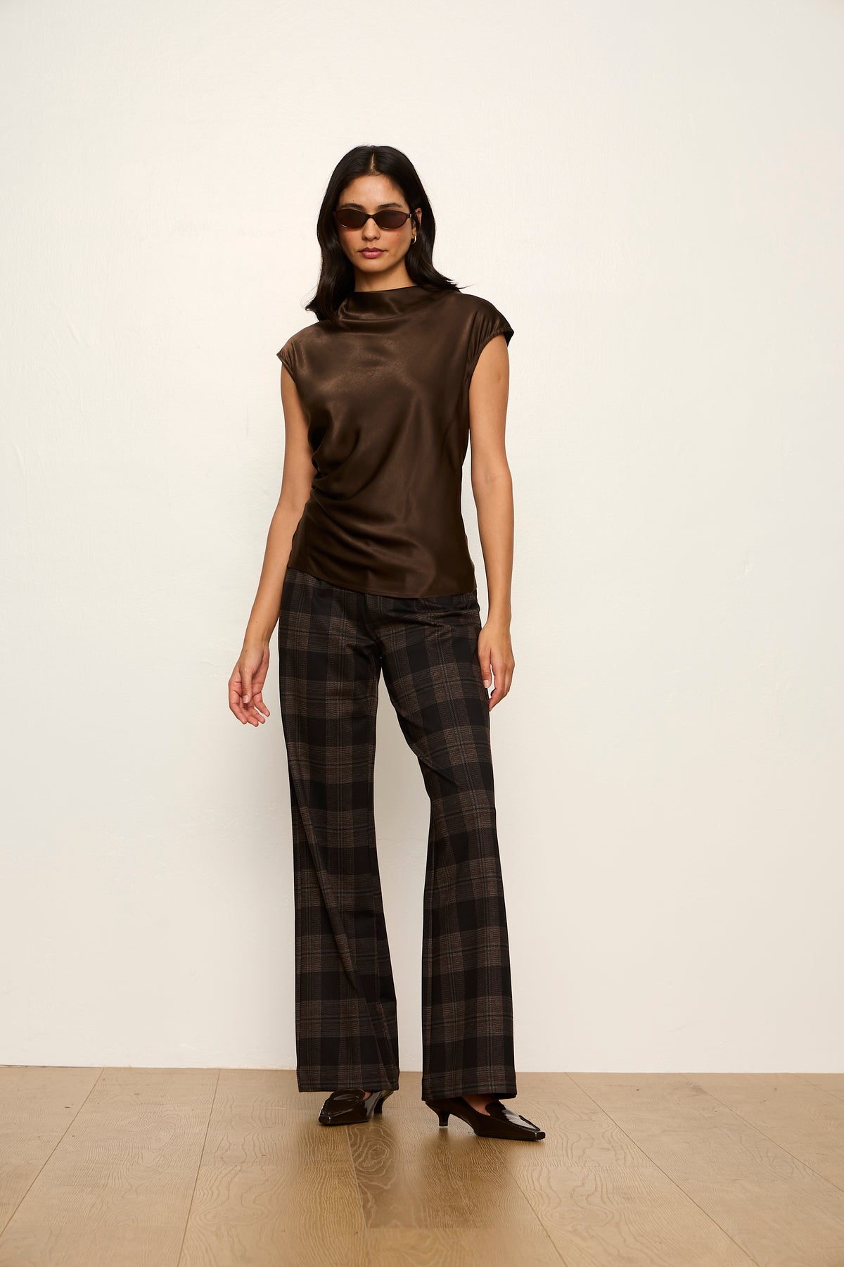 Woman wearing a brown sleeveless top and plaid pants against a white background