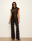 Woman wearing a brown sleeveless top and plaid pants against a white background