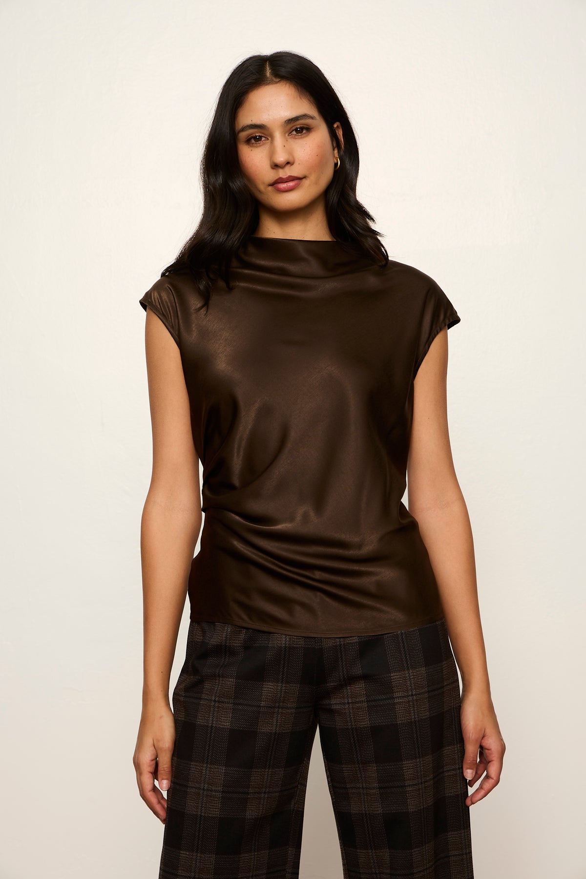 Woman wearing a brown sleeveless top and plaid pants on a white background