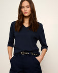 Woman wearing a navy blue outfit with a belt against a plain background