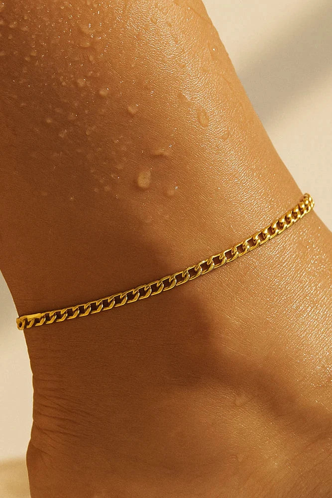 Gold chain anklet on a person's ankle with a neutral background