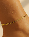 Gold chain anklet on a person's ankle with a neutral background