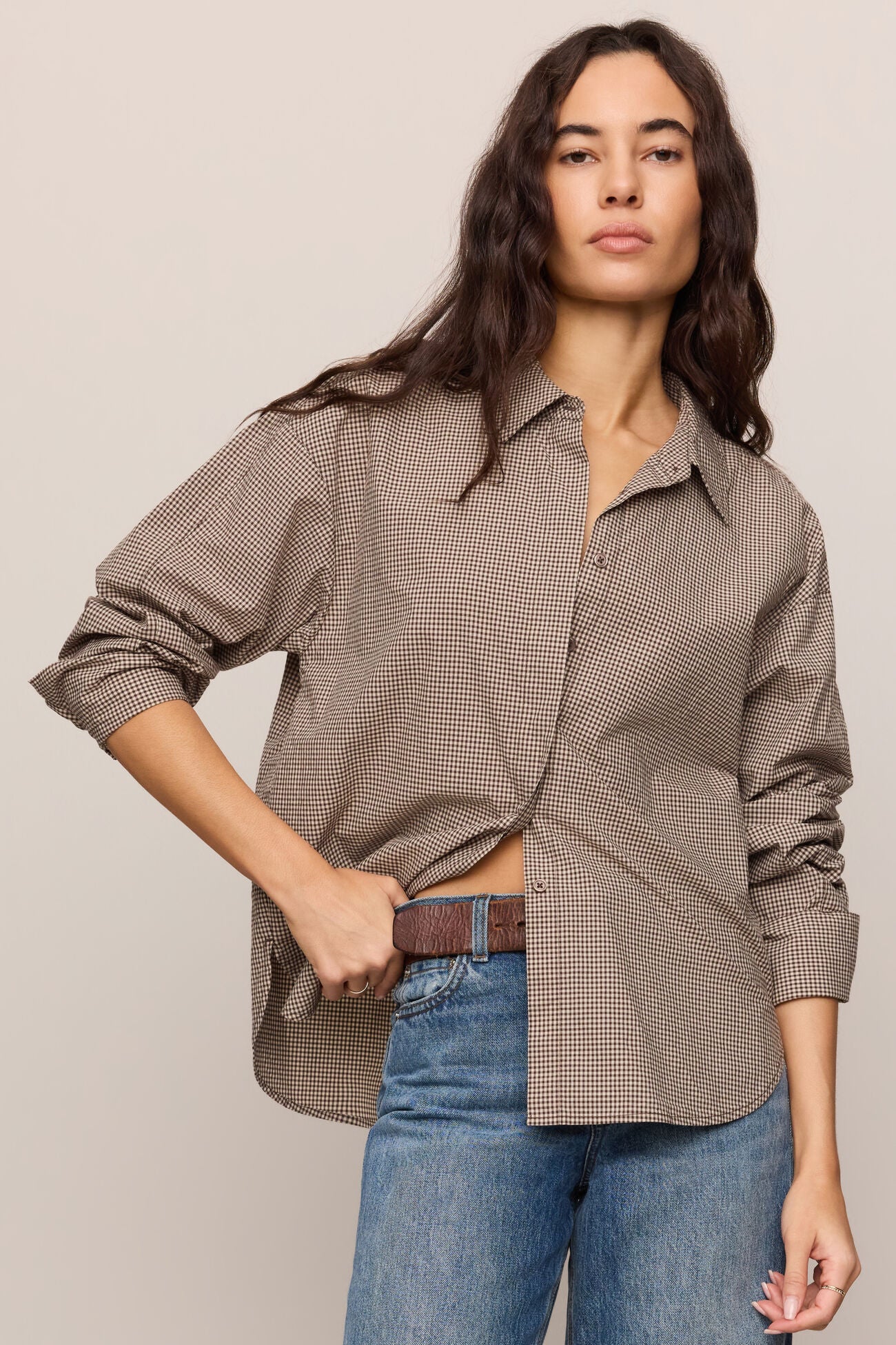 Woman wearing a brown checkered shirt and blue jeans on a beige background