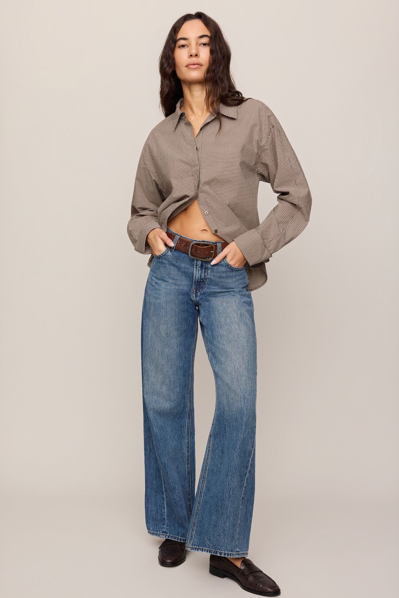 Person wearing a beige shirt and blue jeans on a plain background
