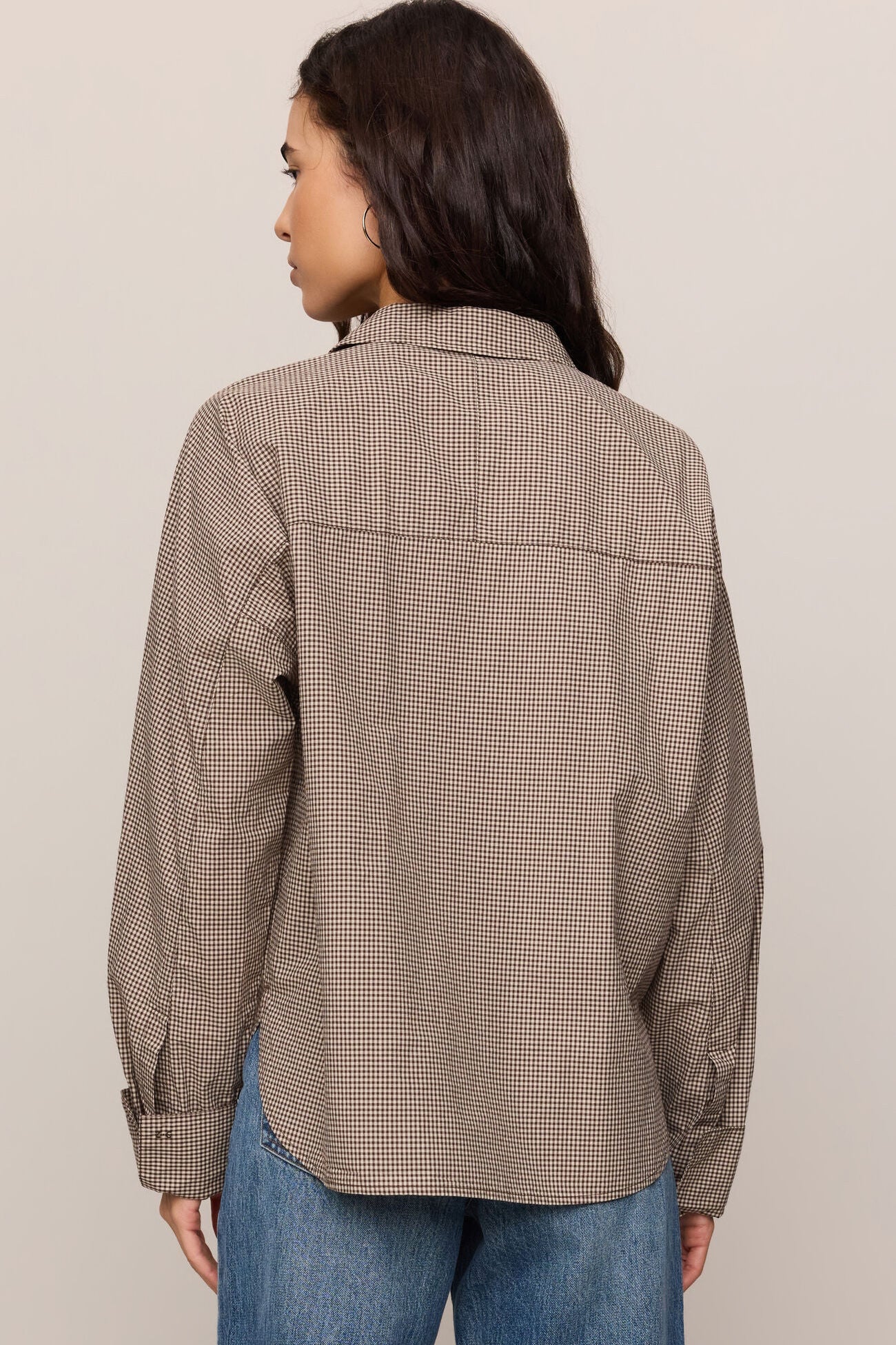 Person wearing a brown checkered shirt and blue jeans against a beige background