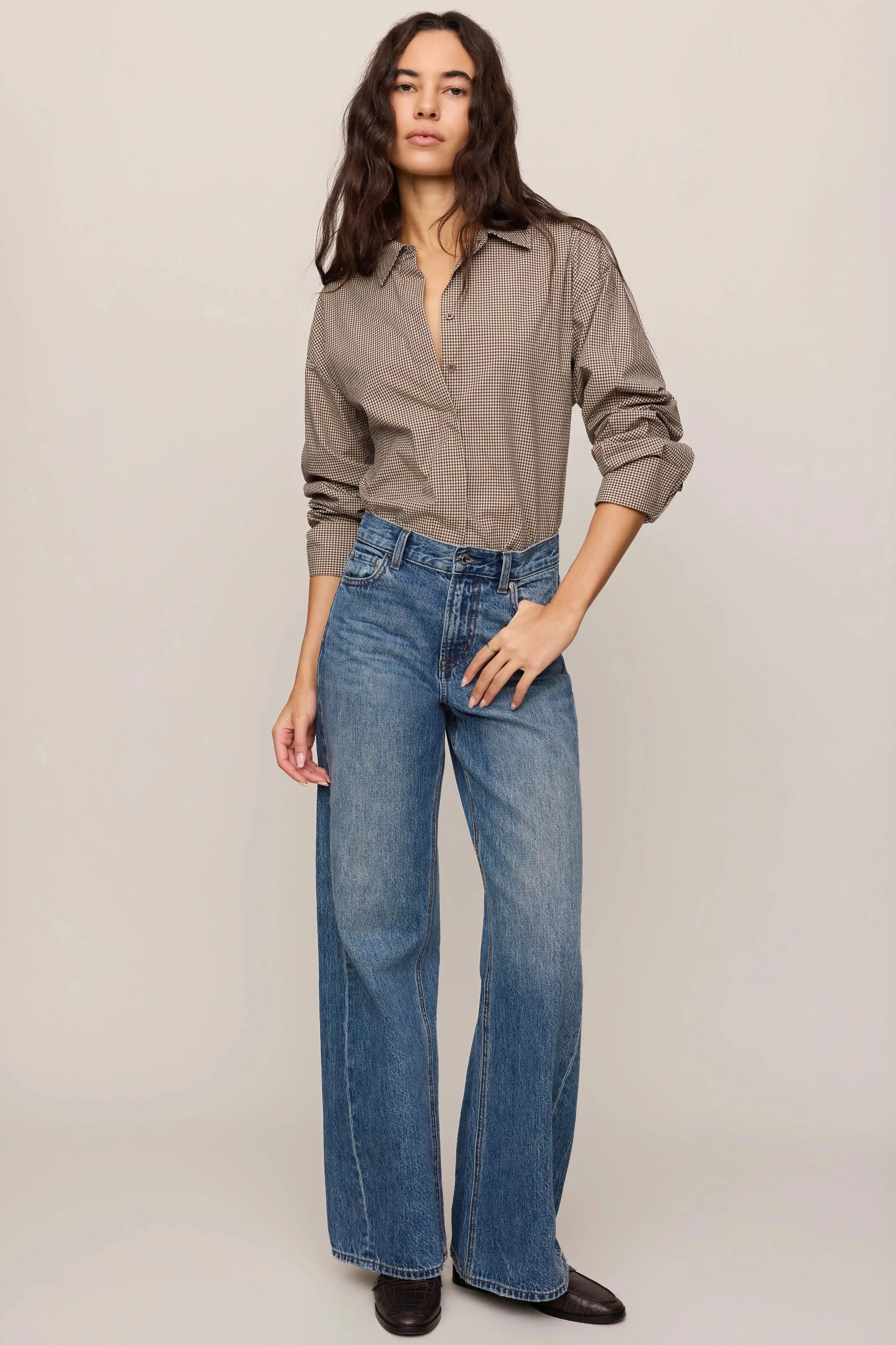 Woman wearing a beige shirt and blue jeans on a plain background