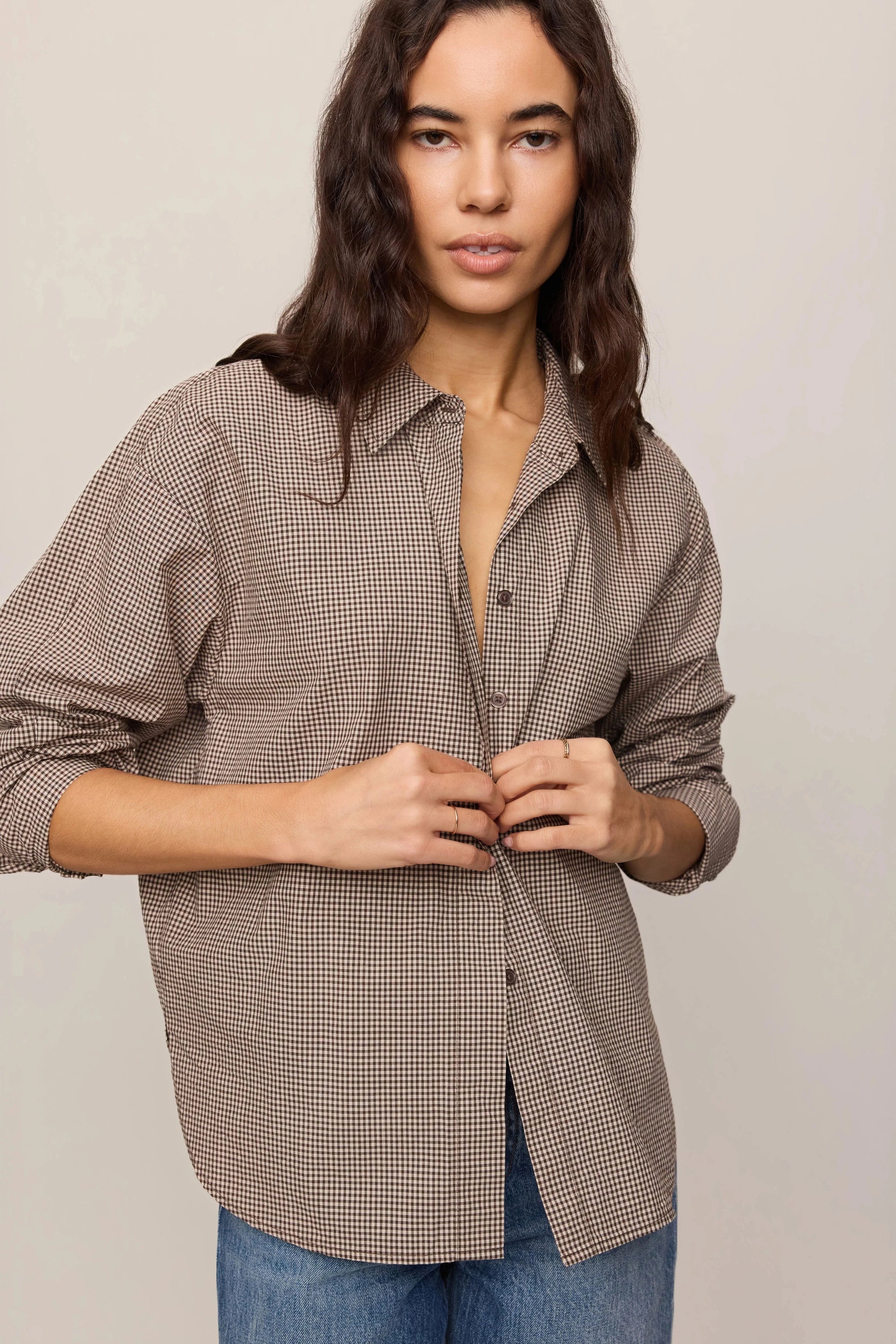 Woman wearing a brown checkered shirt and blue jeans against a plain background