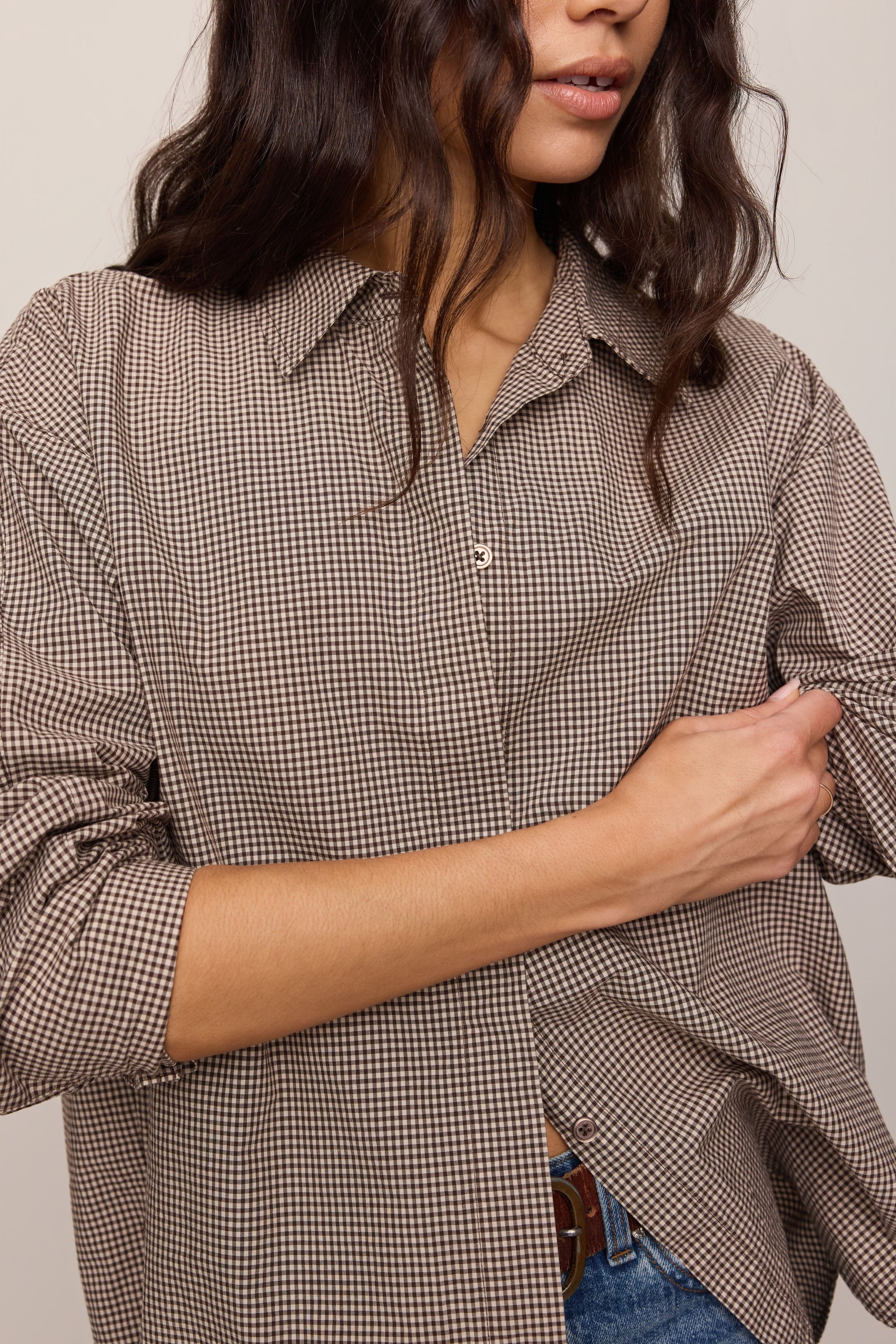 Person wearing a brown checkered shirt with rolled-up sleeves against a neutral background