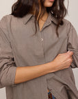 Person wearing a brown checkered shirt with rolled-up sleeves against a neutral background