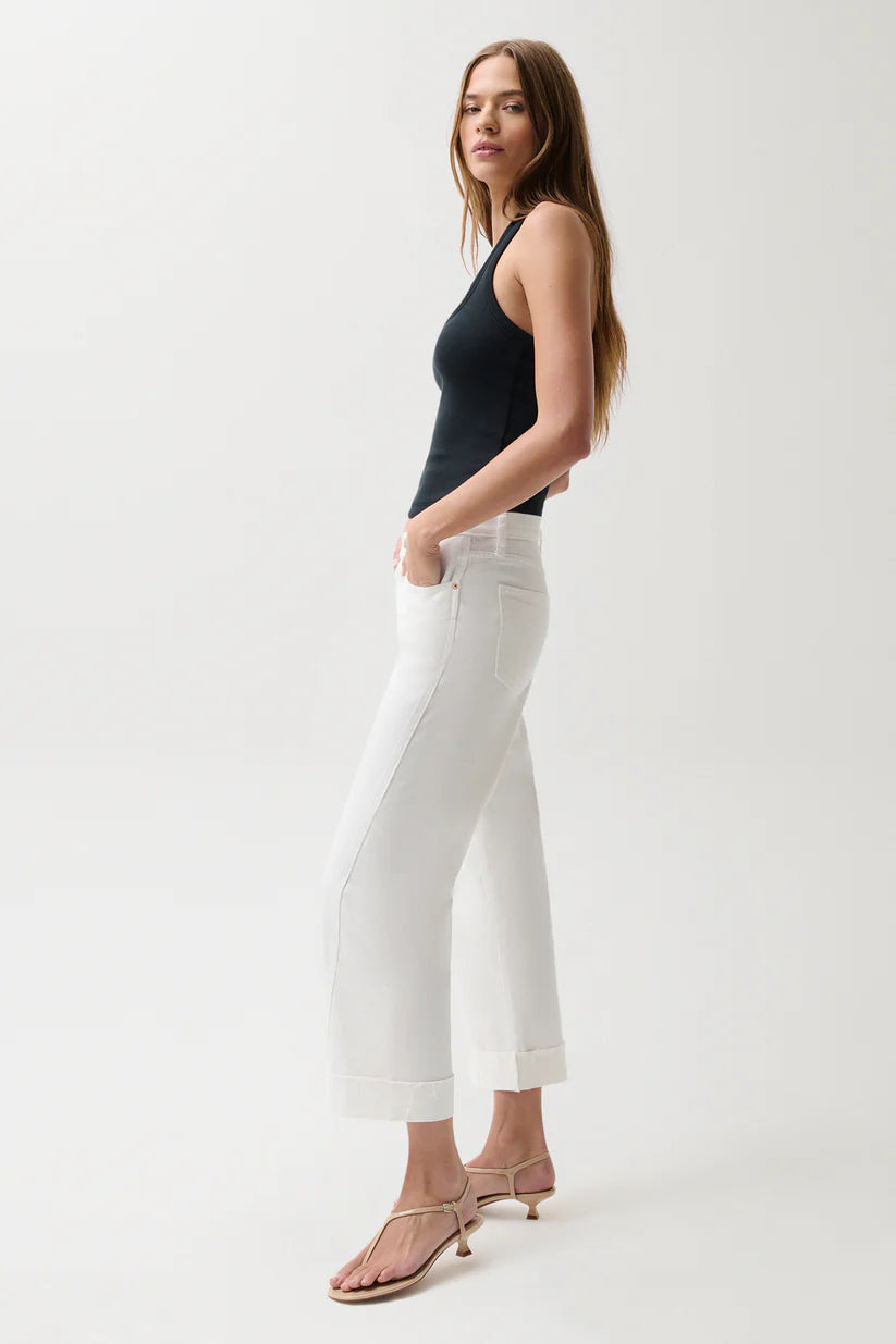 Woman wearing a black sleeveless top and white pants on a white background