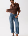 Person wearing a brown poncho and blue jeans on a white background