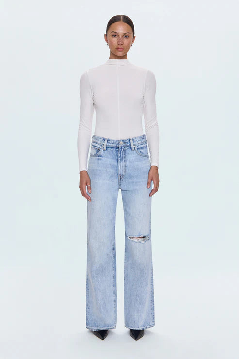 Person wearing a white turtleneck and light blue jeans on a white background