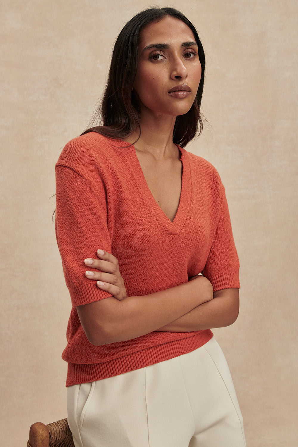 Woman wearing a coral sweater against a beige background