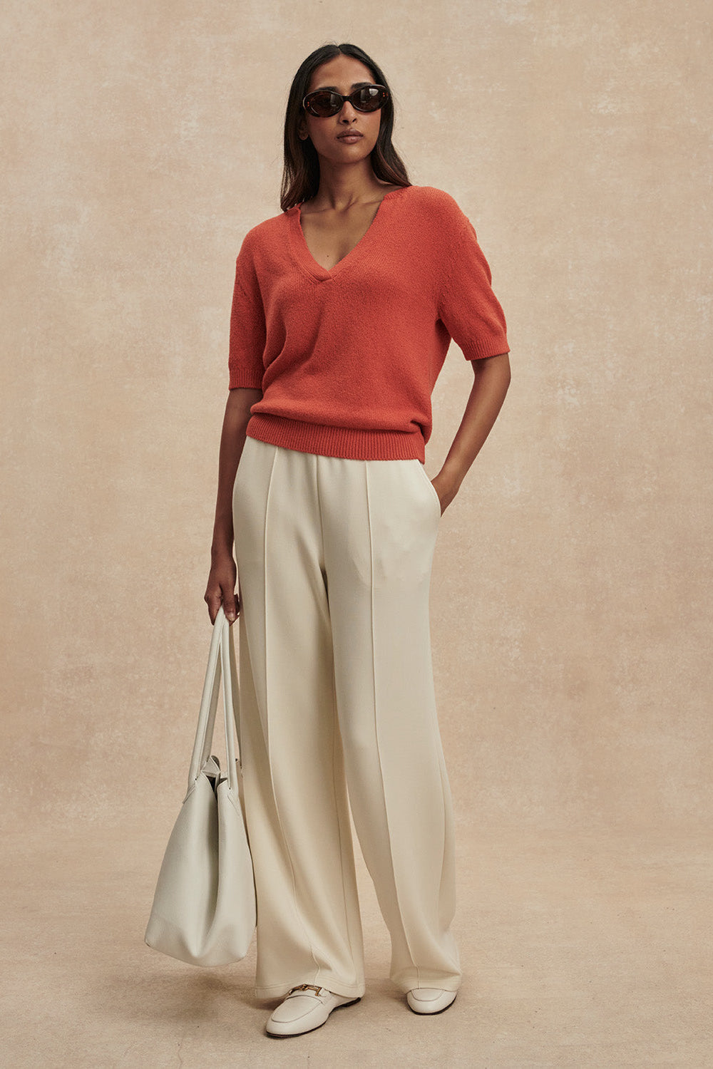 Woman wearing a red sweater and beige pants against a beige background