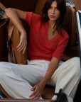 Woman in a red top and white pants sitting inside a car.
