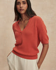 Woman wearing a red sweater and white pants against a beige background
