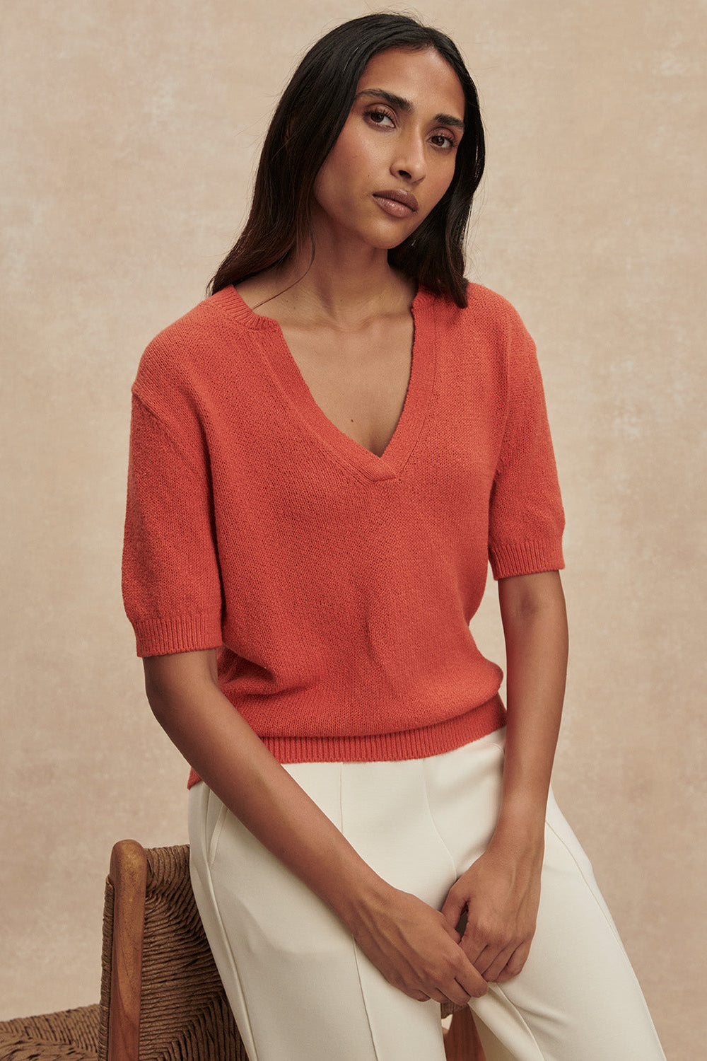Woman wearing a red sweater and white pants against a beige background