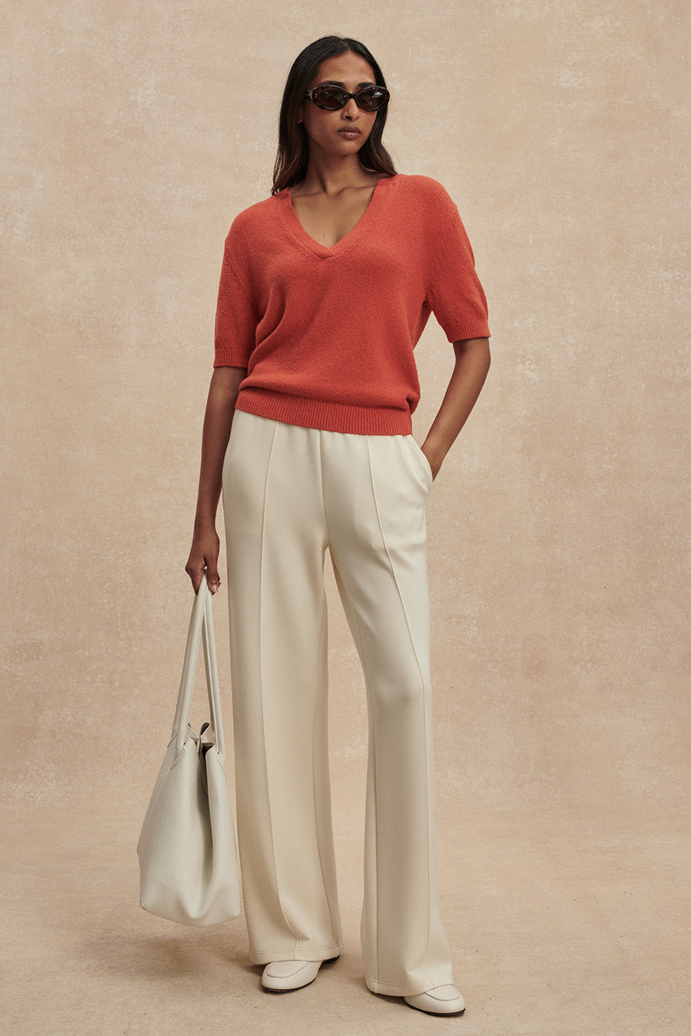 Woman wearing a red sweater and white pants against a beige background