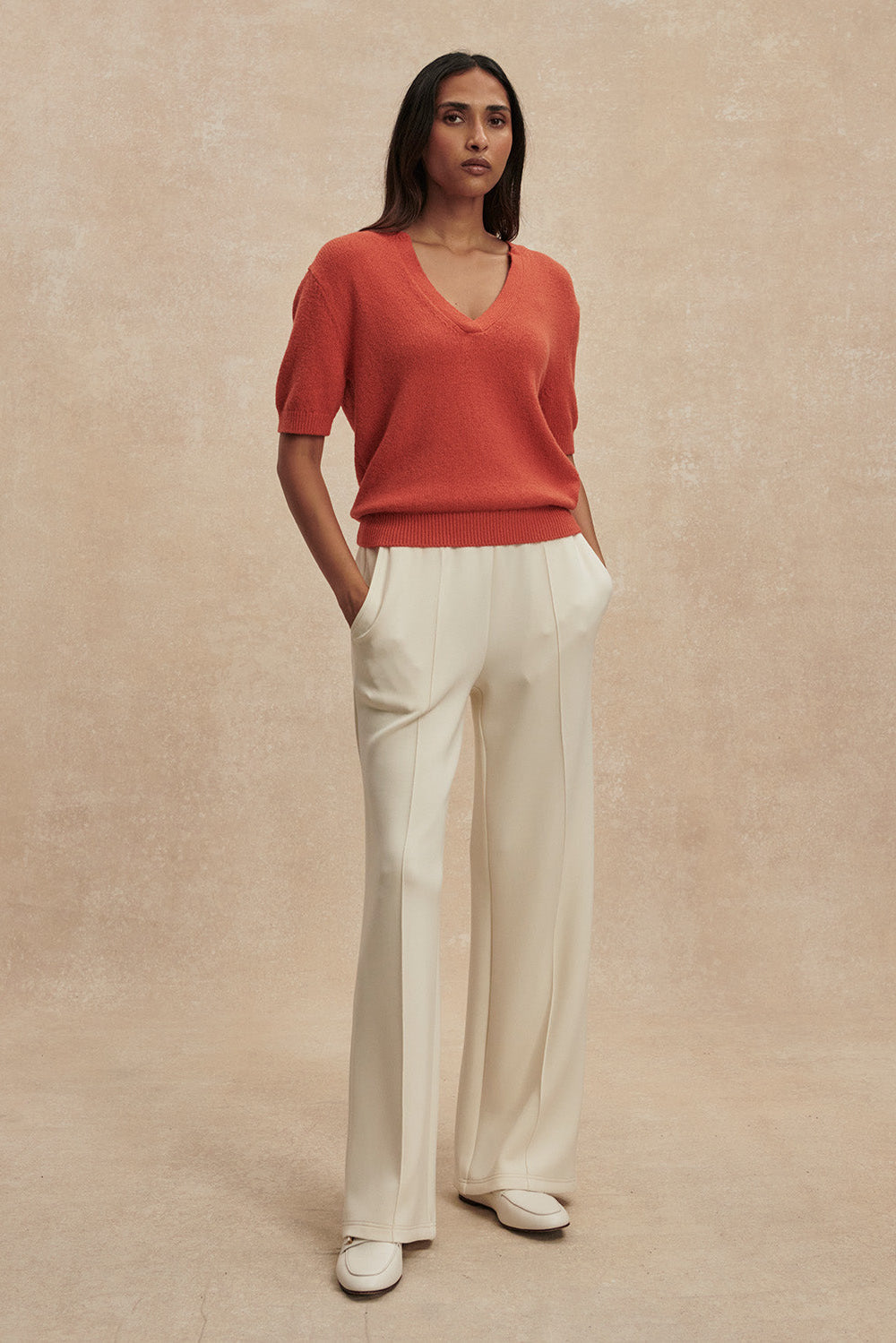 Woman wearing a red sweater and white pants against a beige background