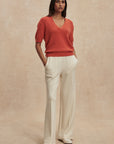 Woman wearing a red sweater and white pants against a beige background