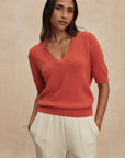 Woman wearing a red sweater and beige pants against a beige background