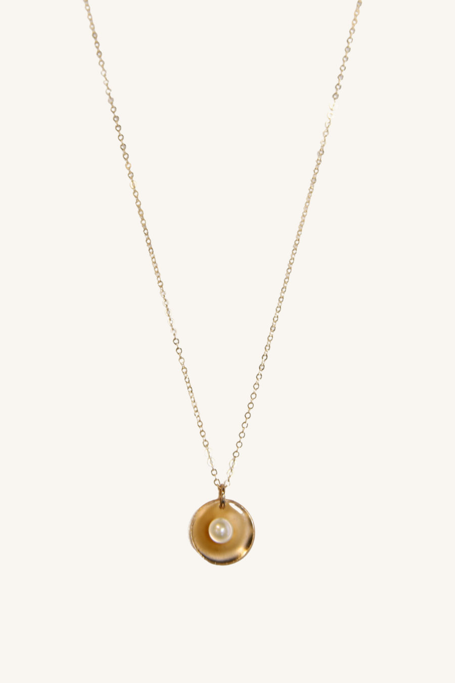 Gold necklace with a circular pendant on a white background