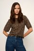 A woman modeling a short-sleeve leopard print top with blue jeans against a plain light background.