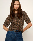 A woman modeling a short-sleeve leopard print top with blue jeans against a plain light background.