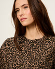 A close-up shot of a woman wearing a brown and black leopard print knit top against a plain light background.