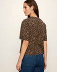 A woman shown from the back wearing a brown and black leopard print short-sleeve top with blue jeans, photographed against a plain off-white studio background.