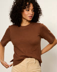 Woman wearing a brown sweater and beige pants against a plain background