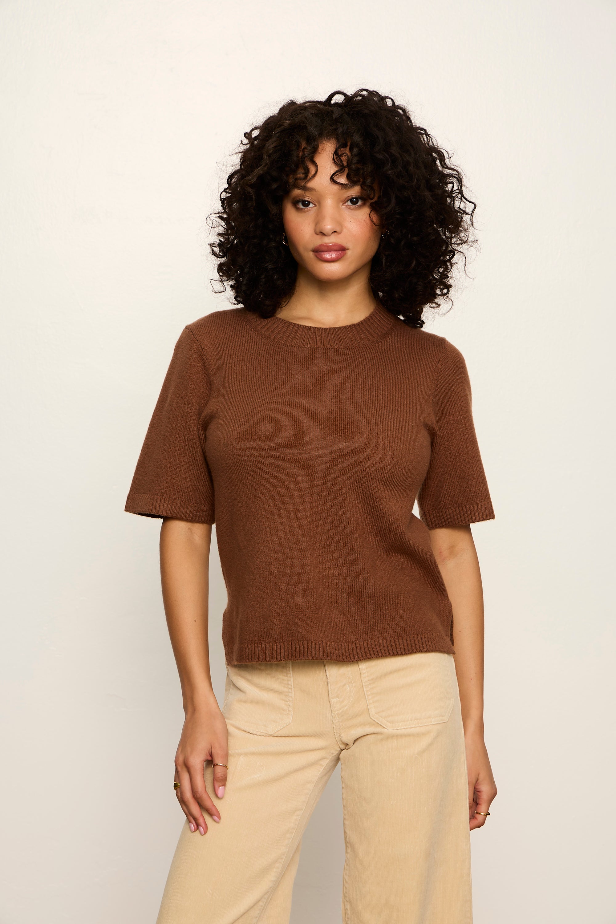 Woman wearing a brown t-shirt and beige pants against a white background