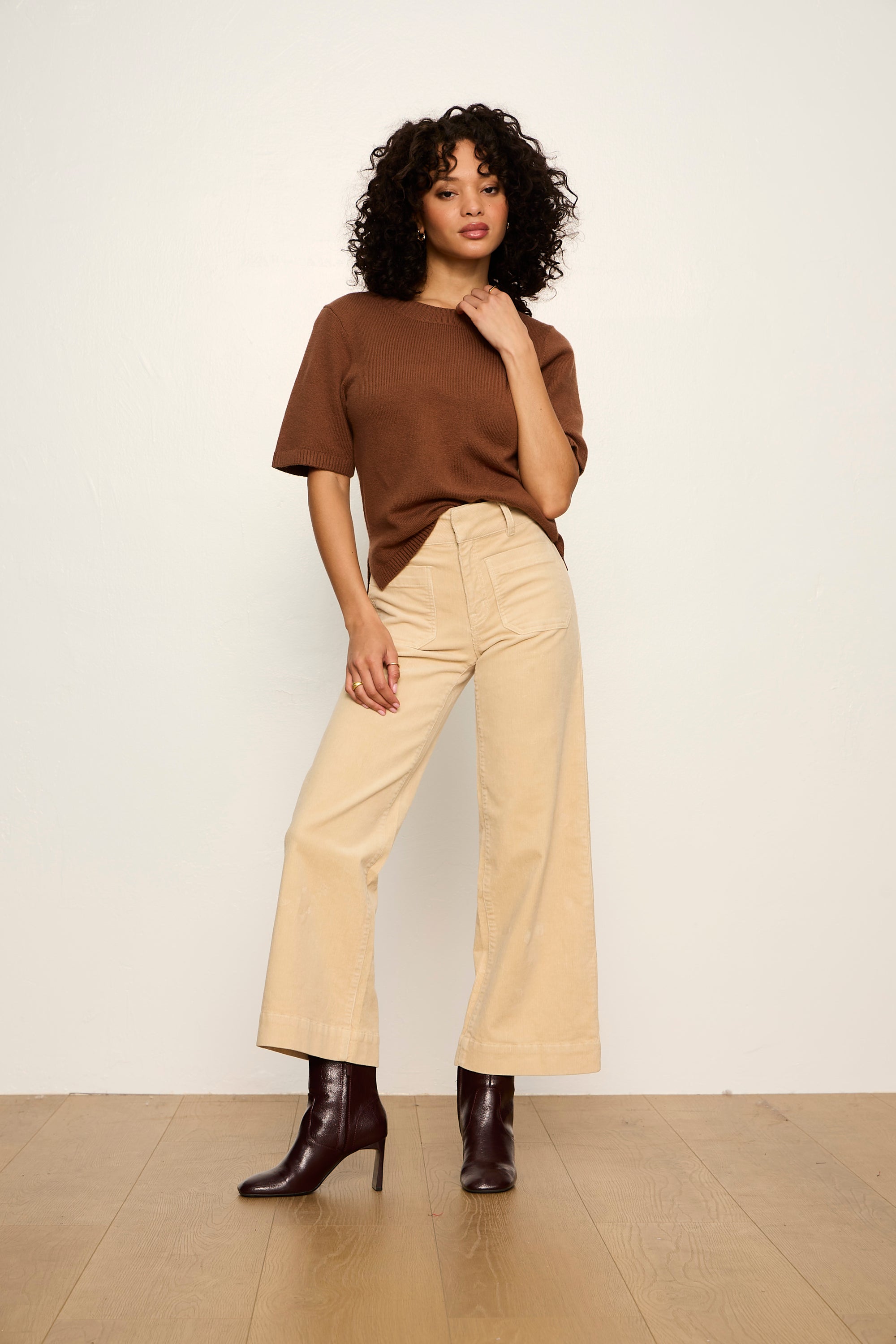 Woman wearing a brown top and beige pants against a white background