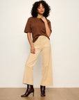 Woman wearing a brown top and beige pants against a white background