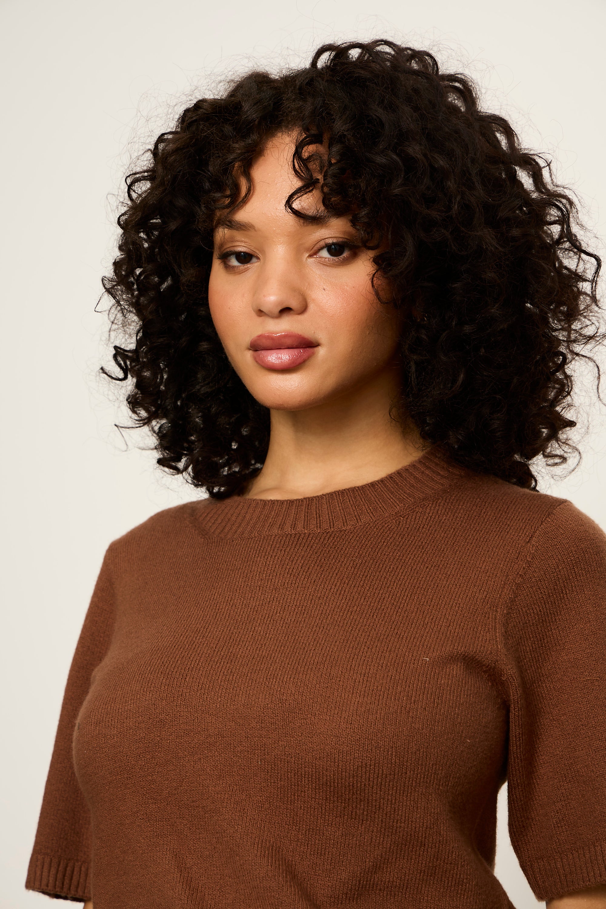 Woman wearing a brown sweater against a plain background