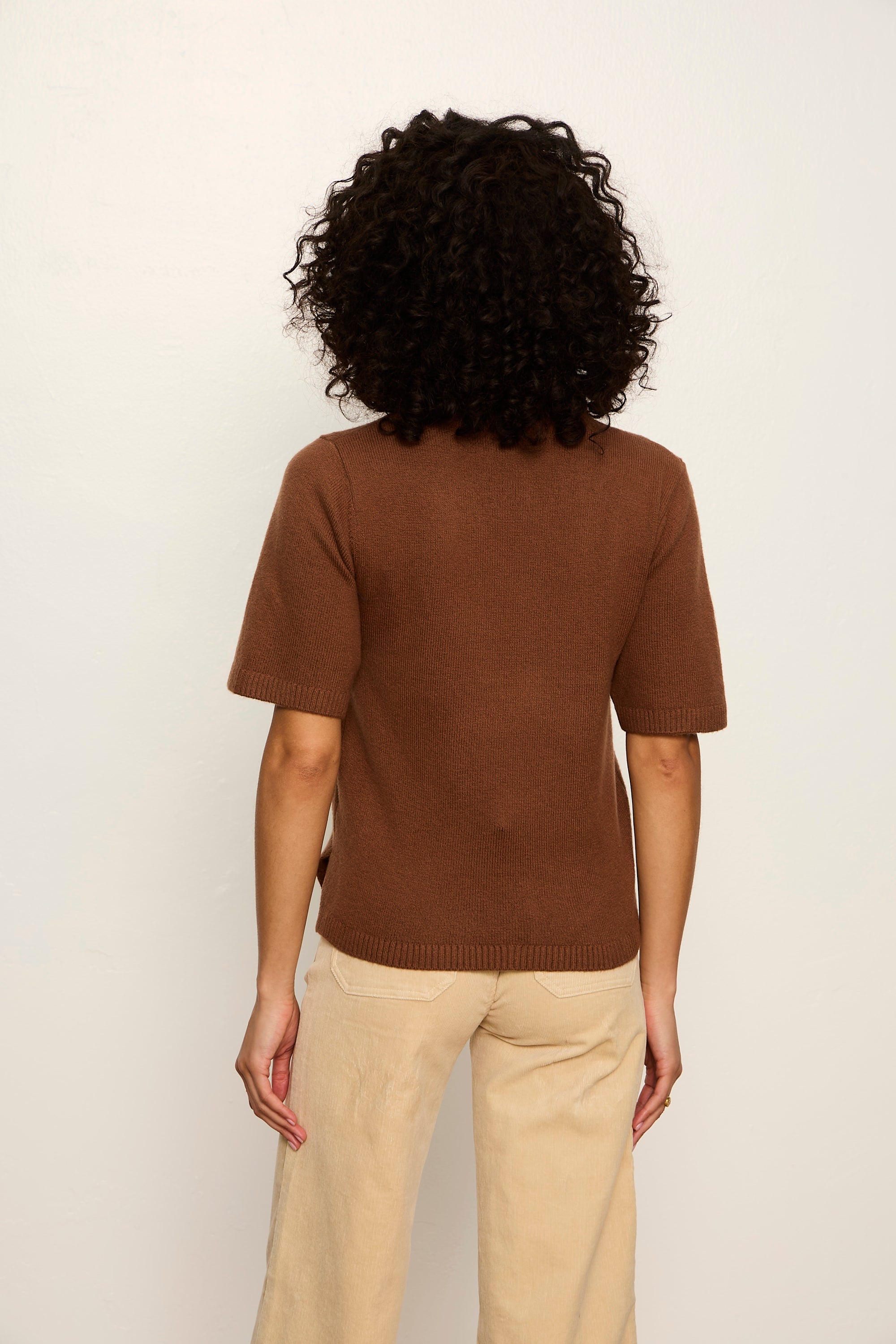Person wearing a brown sweater and beige pants against a white background