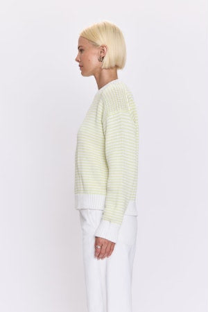 Person wearing a light green striped sweater and white pants on a plain background