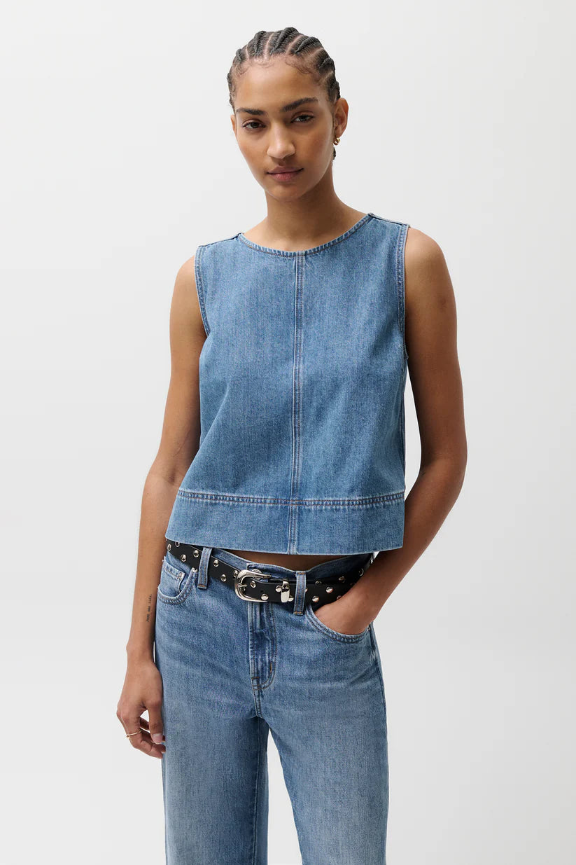 Woman wearing a denim sleeveless top and jeans on a plain background
