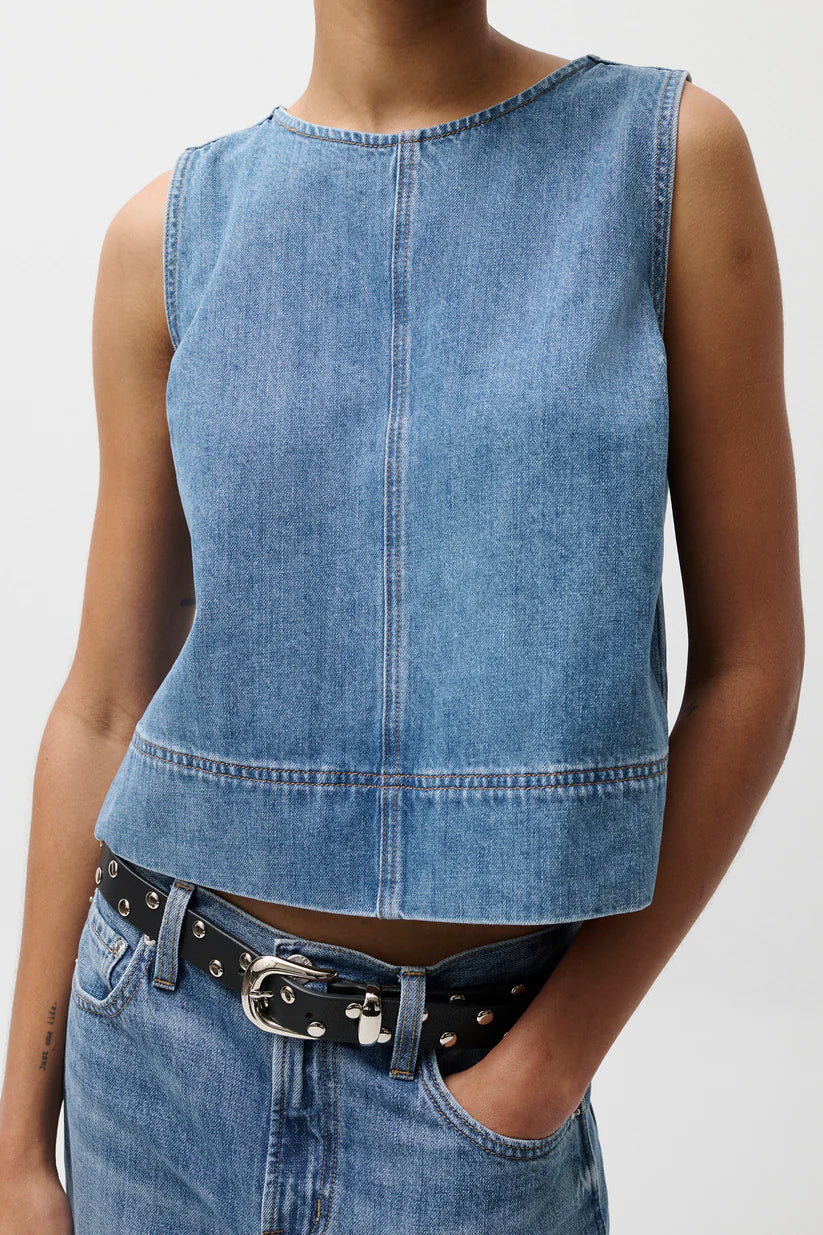 Person wearing a blue denim sleeveless top and jeans on a white background