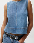 Person wearing a blue denim sleeveless top and jeans on a white background