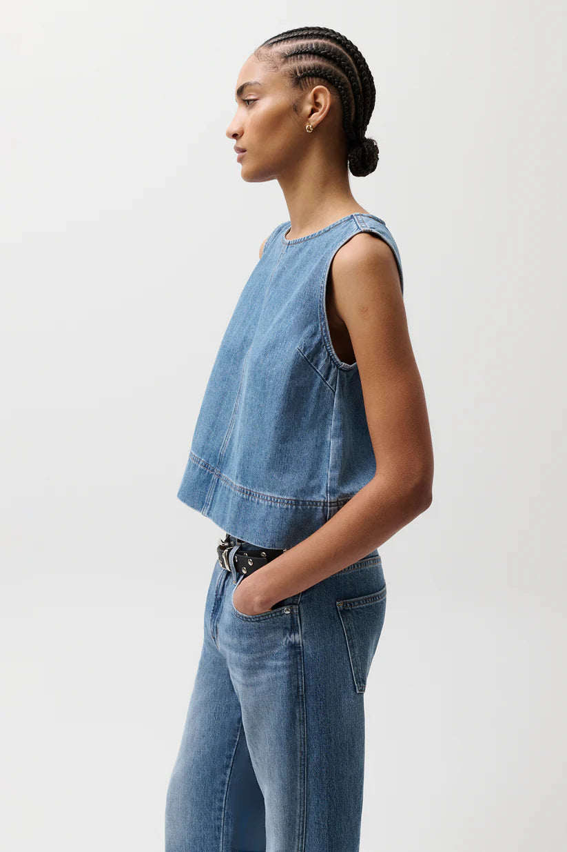 Woman wearing a denim sleeveless top and jeans on a white background