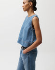 Woman wearing a denim sleeveless top and jeans on a white background