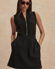 Woman wearing a black sleeveless dress with a zipper on a beige background
