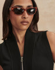 Woman wearing sunglasses and a black sleeveless top against a beige background